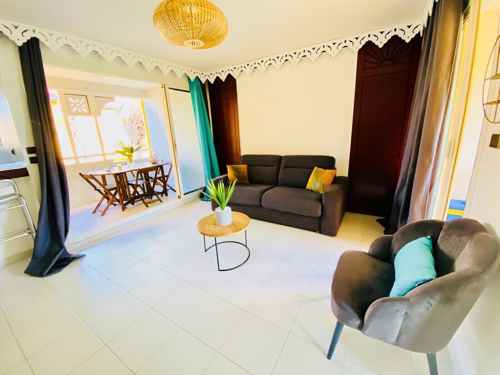 A living room with a sofa, a chair, a small table with a plant, and a dining area with a table and chairs.