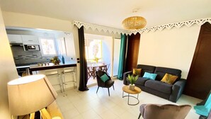 A modern living room with a sofa, armchairs, a coffee table, and a lamp. There is a kitchen area with a microwave and cabinets. - HamO Cosy: Sainte Anne apartment (Sainte Anne)