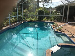 An indoor swimming pool with clear blue water, surrounded by a glass enclosure, and various plants and trees visible outside. - Private Florida Pool Home (Palm Bay)