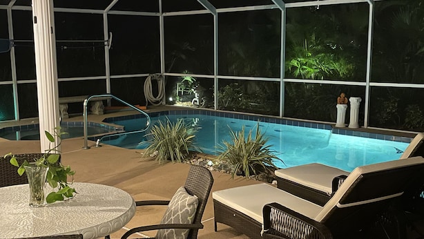 Un espace piscine intérieure doté d’une paroi vitrée, de chaises longues, d’une table avec un vase en verre et de plantes en pot.