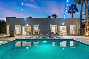 A modern house with a swimming pool, outdoor seating, and string lights.