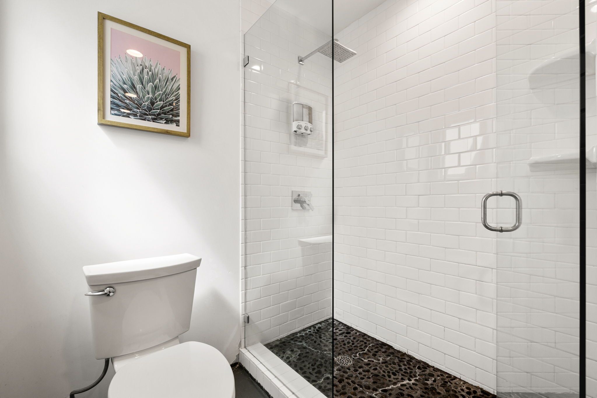 Un baño con inodoro, ducha con puerta de vidrio y pared con azulejos.