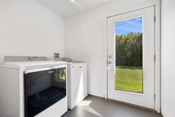 A laundry room with two white washing machines and a door leading to a grassy outdoor area.