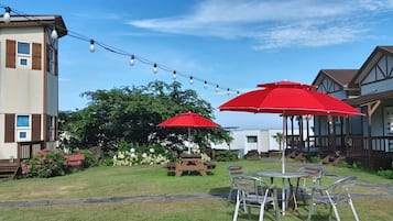A courtyard with picnic tables and red umbrellas, surrounded by houses with Tudor-style architecture.