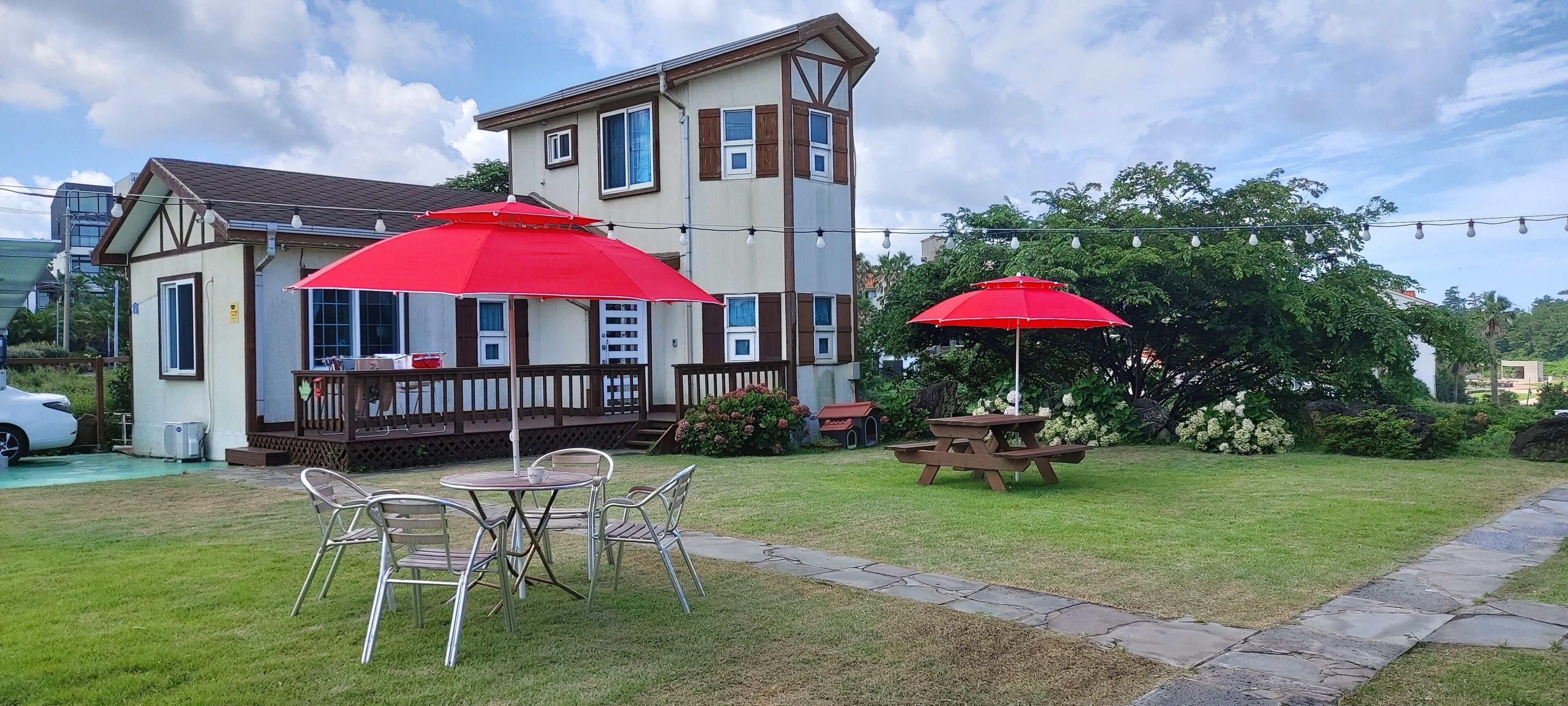 Une cour arrière avec une table de pique-nique et des chaises, un parasol rouge et une maison dotée d’une terrasse.