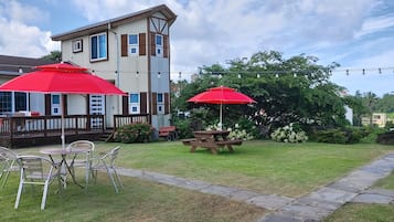 Une cour arrière avec une table de pique-nique et des chaises, un parasol rouge et une maison dotée d’une terrasse.