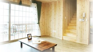 Quarto com paredes de madeira e uma janela grande com vista para o exterior. Há um banco de madeira com um porta-retrato sobre ele.