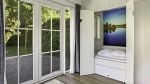 Een slaapkamer met een groot schuifglas dat uitkomt op een tuin, een bed met uitzicht op een meer, en een schilderij van een zonsondergang.