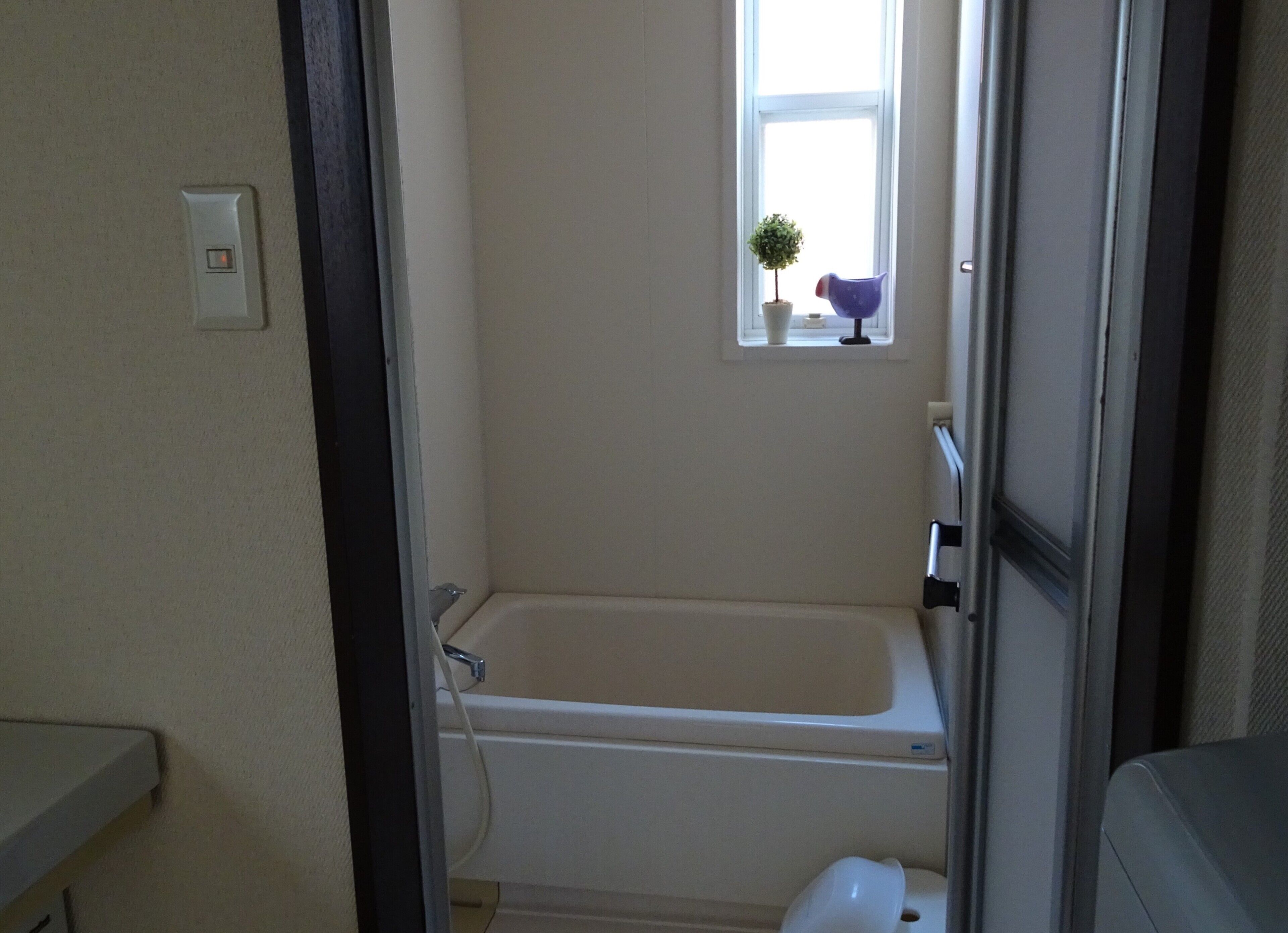 A small bathroom with a bathtub, a window, and a potted plant.