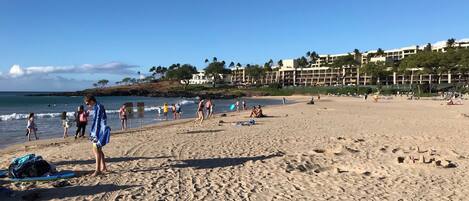 Una playa arenosa con huellas, algunas personas y un edificio al fondo.