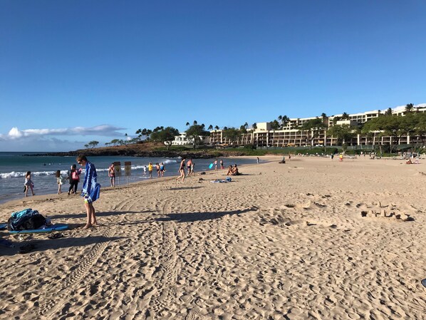 En sandstrand med fotspår, några få personer och en byggnad i bakgrunden.