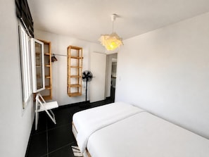 Ein Schlafzimmer mit einem Bett, einem Ventilator, einer Holzleiterregal und einer Tür zu einem Badezimmer.