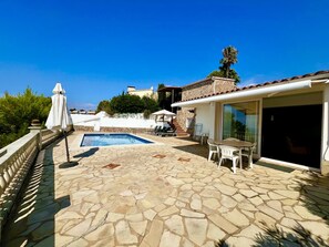 Ein Poolbereich mit Steinböden, einem Tisch mit Stühlen und einer überdachten Sitzgelegenheit mit Sonnenschirmen.
