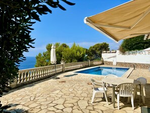 A pool area with a stone patio, white chairs, and a white umbrella.