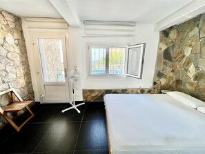 Ein Schlafzimmer mit einem Bett, einem Sessel, einem Ventilator und einer Tür, die auf einen Balkon führt.