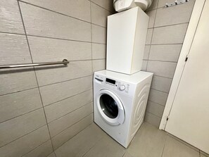 A compact, modern laundry room with a front-loading washing machine, a white cabinet above it, and a metal handrail.