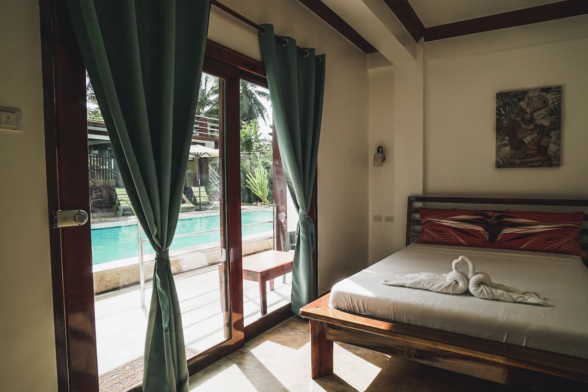 A bedroom with a bed, a painting, and a view of a swimming pool through a glass door.