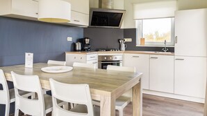 Une cuisine moderne avec des meubles blancs, une table à manger en bois et un micro-ondes encastré.