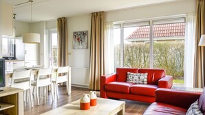 Un salon moderne avec un canapé rouge, une table basse en bois et un coin repas avec des chaises blanches.