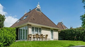 Une maison avec un toit en pente, un patio couvert avec des chaises et une jetée en bois qui s’avance sur l’eau.