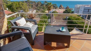 A balcony with wicker furniture, a small table, and a view of the sea and greenery. - Berganti by Interhome (Tossa de Mar)