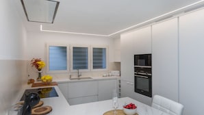 A modern kitchen with white cabinetry, a built-in oven, and a microwave. - Berganti by Interhome (Tossa de Mar)