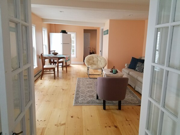 A spacious living area with a wooden floor, a dining table with chairs, a sofa, and a fluffy chair. - Beach Vibes & Fun Colors in the Seashell Suite (Onset)