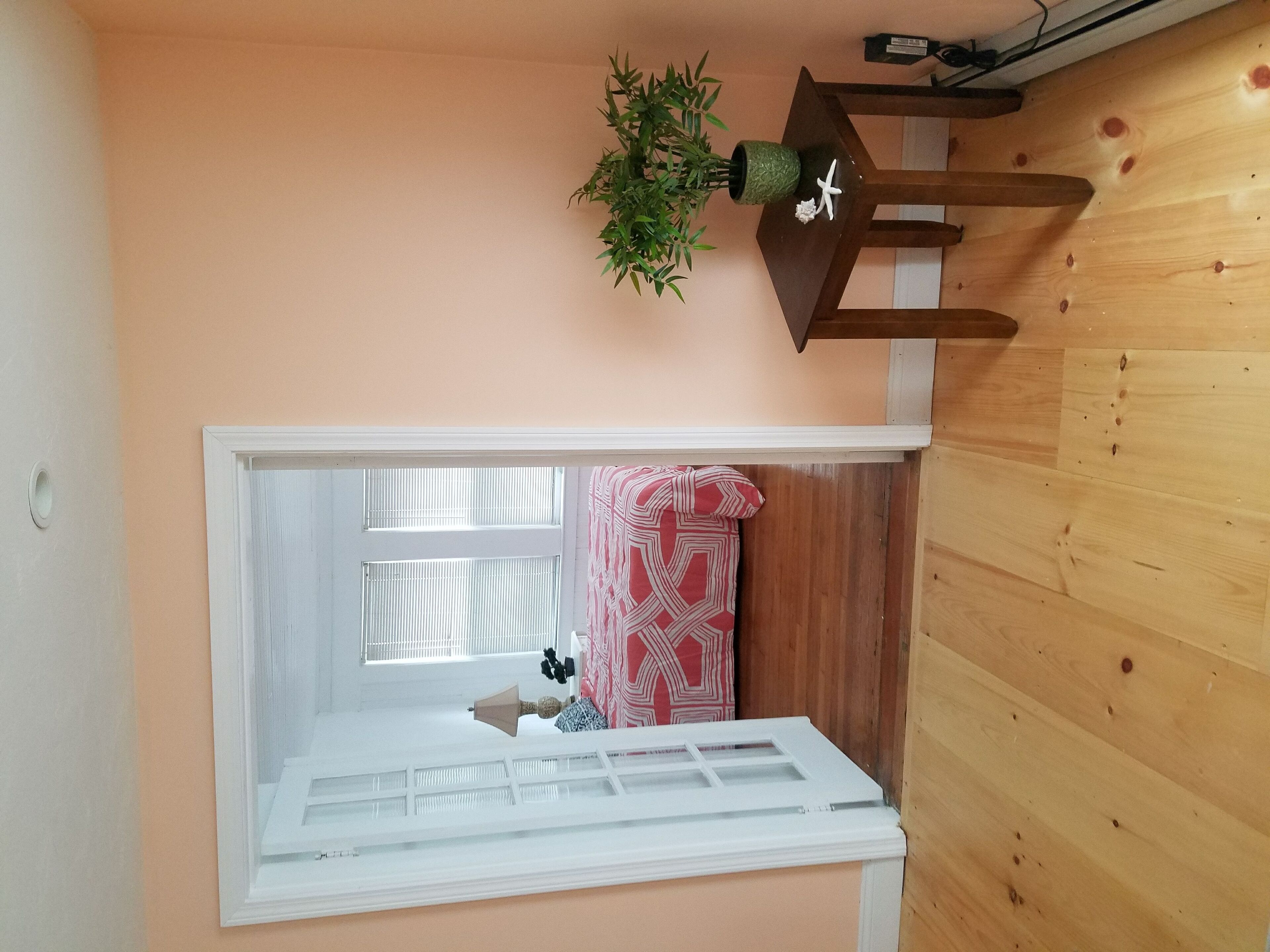 A room with a wooden floor, a small table with a plant, and a window with blinds.