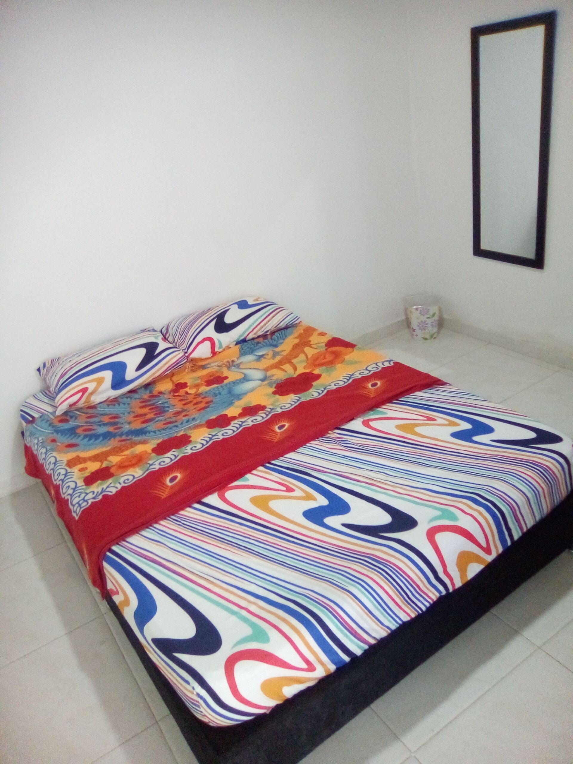 Una cama con una colcha y almohadas de estampado colorido, una mesita de noche con un vaso y un espejo en la pared.
