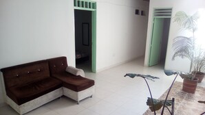A room with a brown sofa, a tiled floor, a potted plant, and a doorway leading to another room. - Casa Love (Guadalajara de Buga)