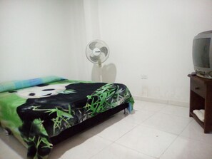 A room with a bed, a standing fan, and a television on a wooden stand. - Casa Love (Guadalajara de Buga)