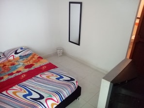 A bedroom with a bed, a bedside table, a mirror, and a trash bin. - Casa Love (Guadalajara de Buga)