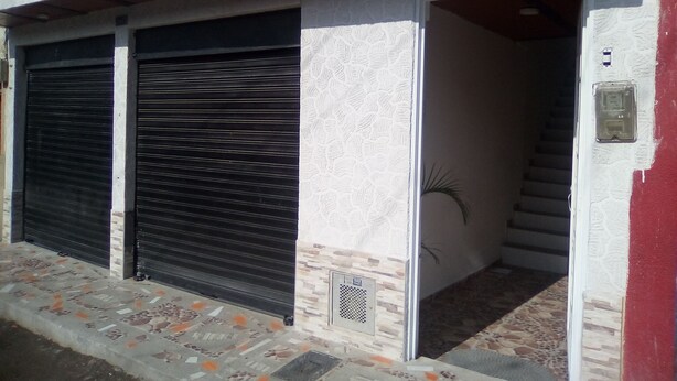 A building with two closed shuttered doors, a staircase leading to an upper level, and a small vent on the wall. - Casa Love (Guadalajara de Buga)