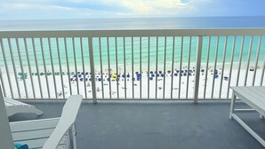 Een balkon met uitzicht op een strand met parasols en mensen.