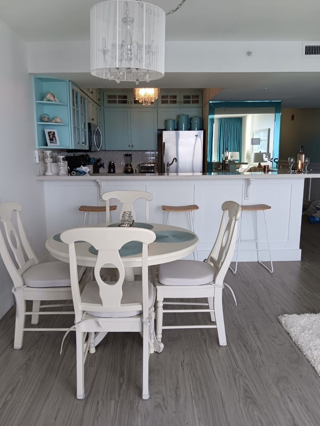 A modern kitchen with a central island, white chairs, and a chandelier.
