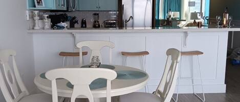 A modern kitchen with a central island, white chairs, and a chandelier.