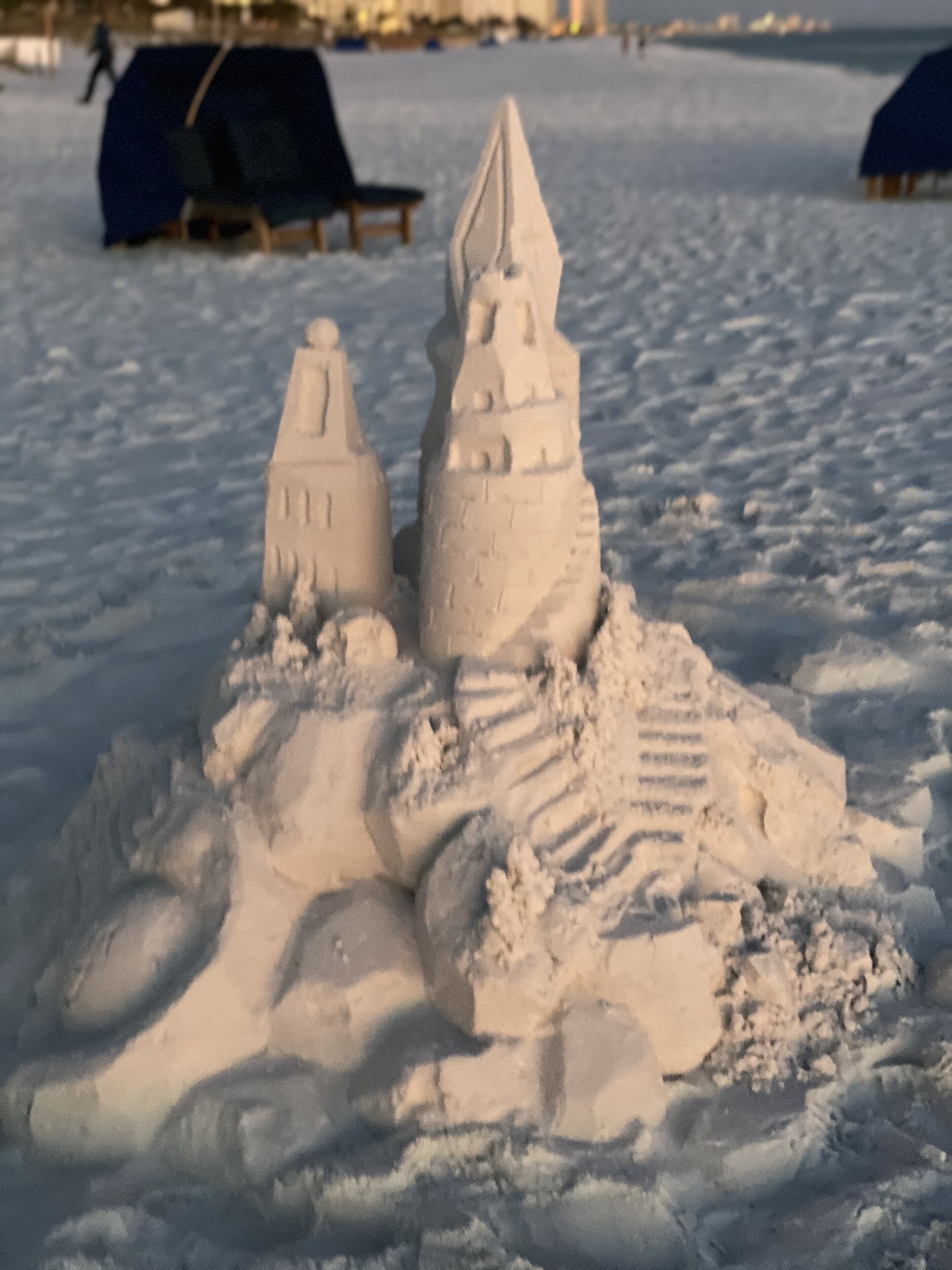 A sandcastle with two towers and a staircase, surrounded by snow.