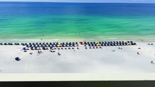 Een strand met rijen parasols en mensen.