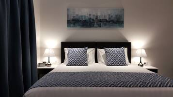 Habitación de hotel con una cama grande, dos mesitas de noche, dos lámparas, un cuadro de paisaje urbano en la pared y una cortina oscura.