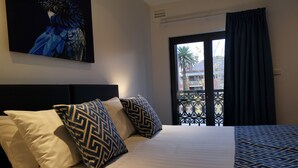 Une chambre d’hôtel avec un lit, des coussins à motifs, un tableau au mur et une vue sur les bâtiments par la fenêtre.