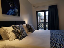 Habitación de hotel con cama, almohadones estampados, un cuadro en la pared y vistas de edificios por la ventana.