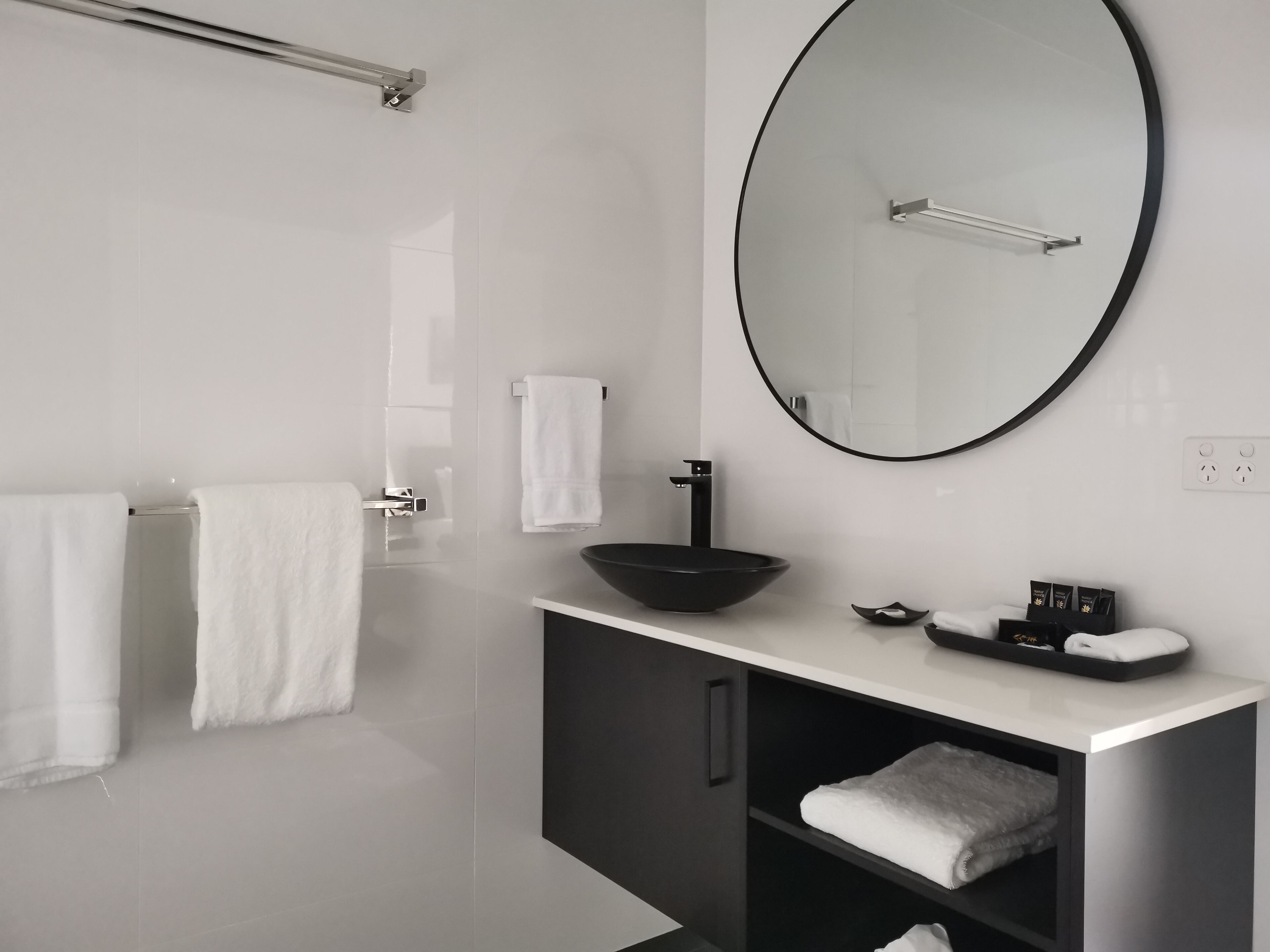 A modern bathroom with a large mirror, a black sink, and two white towels on a rack.