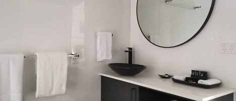 A modern bathroom with a large mirror, a black sink, and two white towels on a rack.