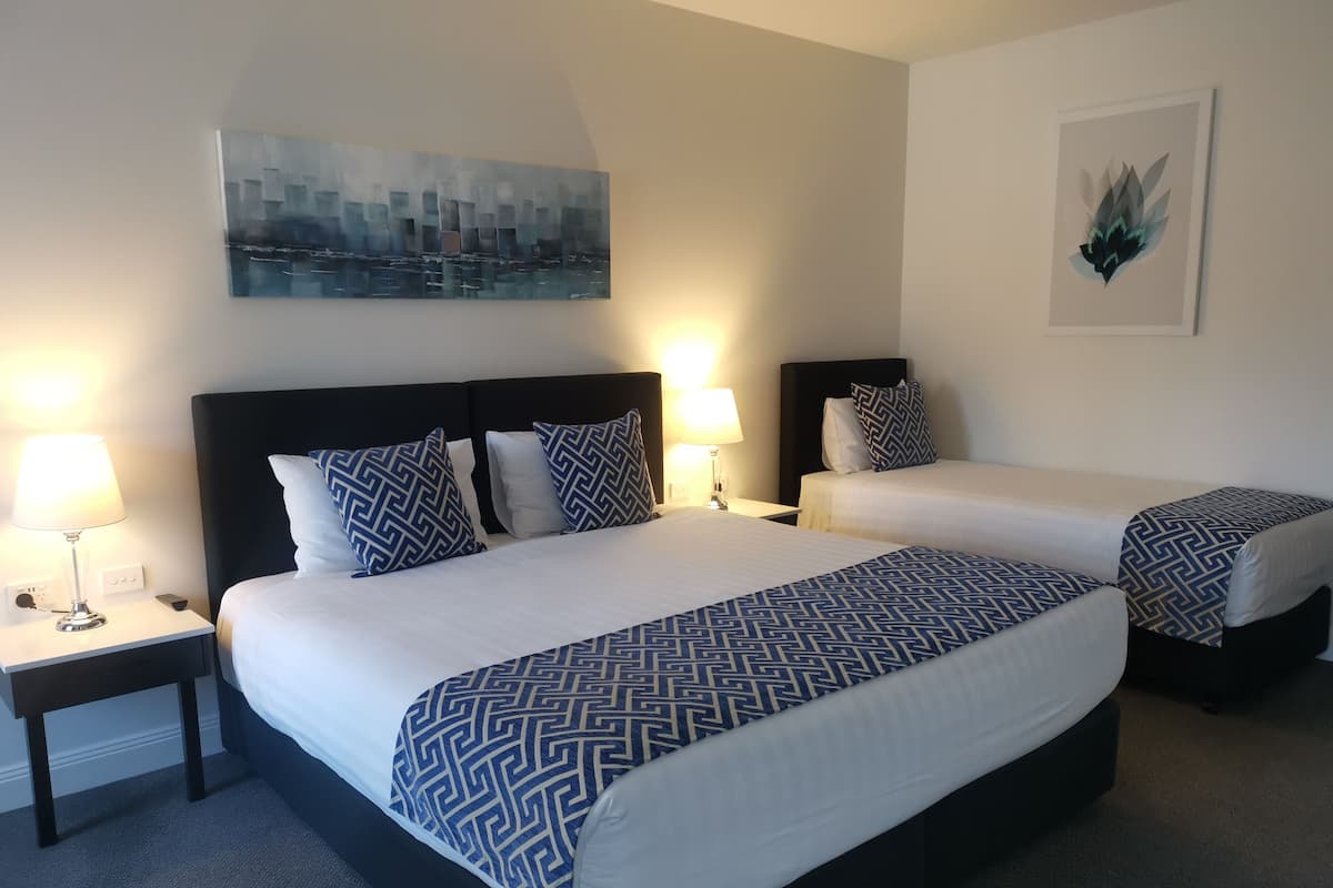 Una habitación de hotel con dos camas, cada una con una colcha estampada, una mesita de noche con lámpara y un cuadro en la pared.