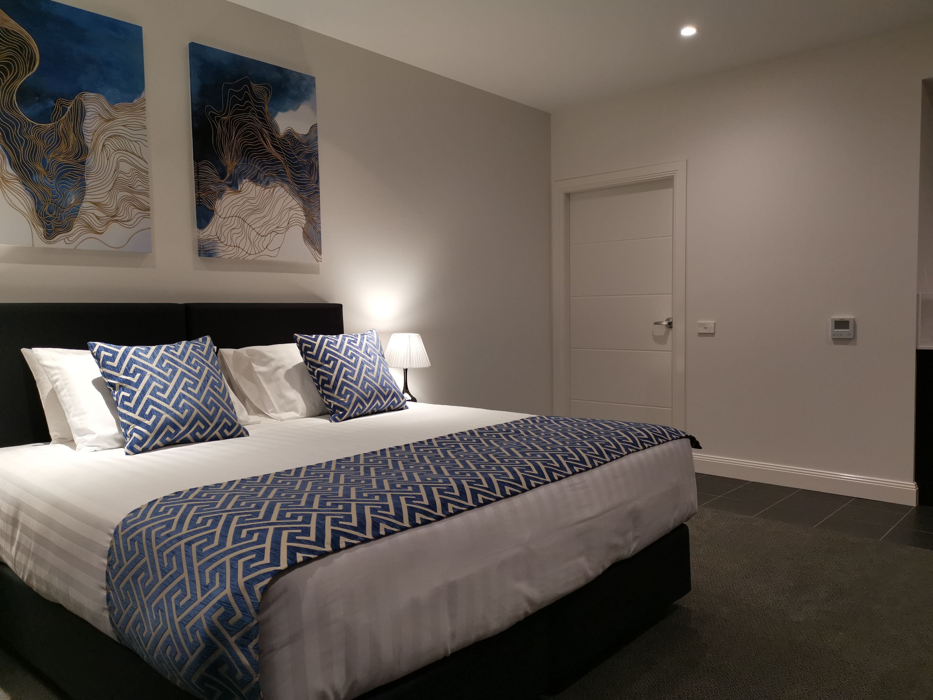 Un dormitorio moderno con una cama grande, un cabecero oscuro y dos obras de arte abstractas en la pared.