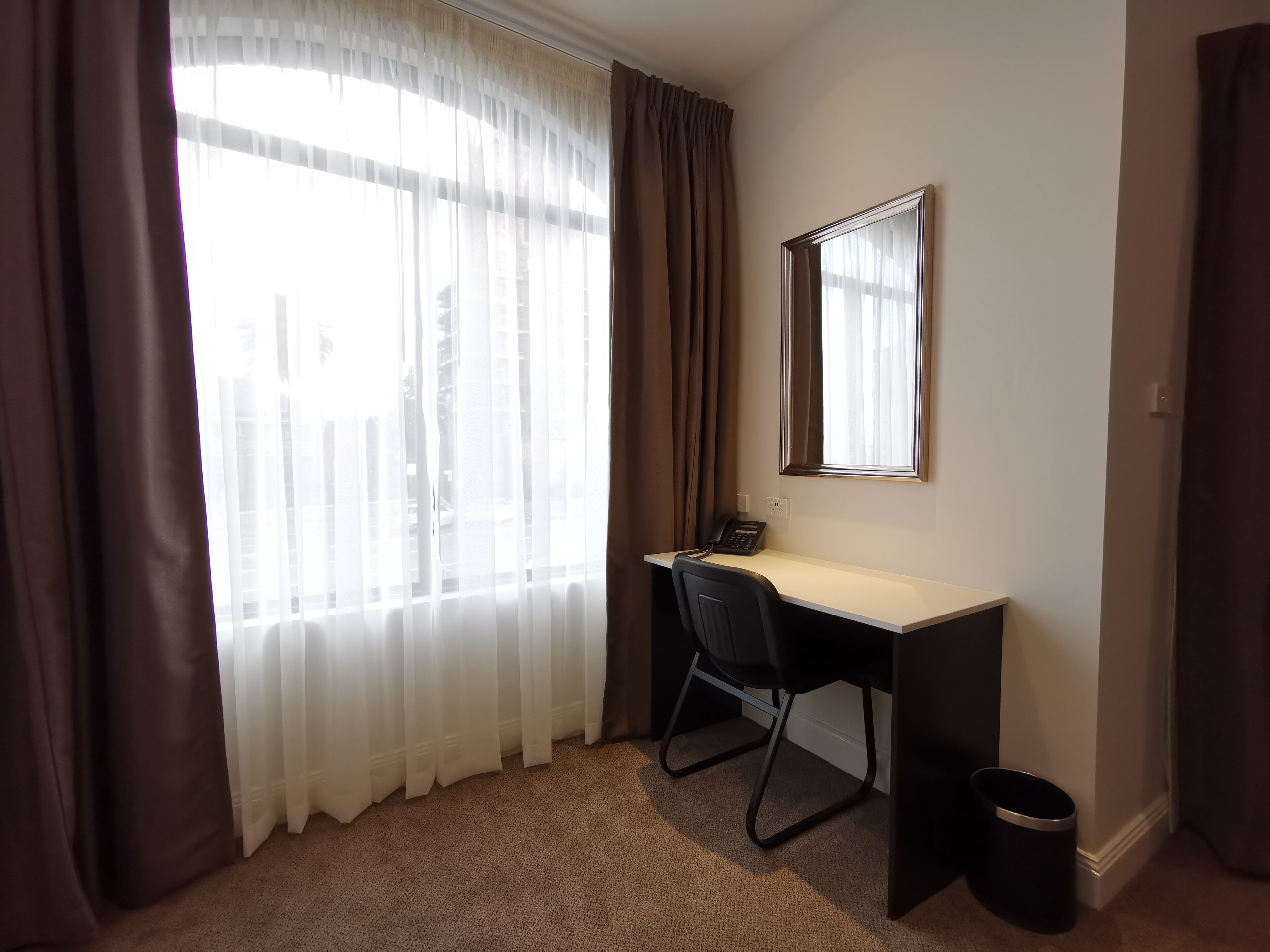 A hotel room with a desk, chair, and a telephone.