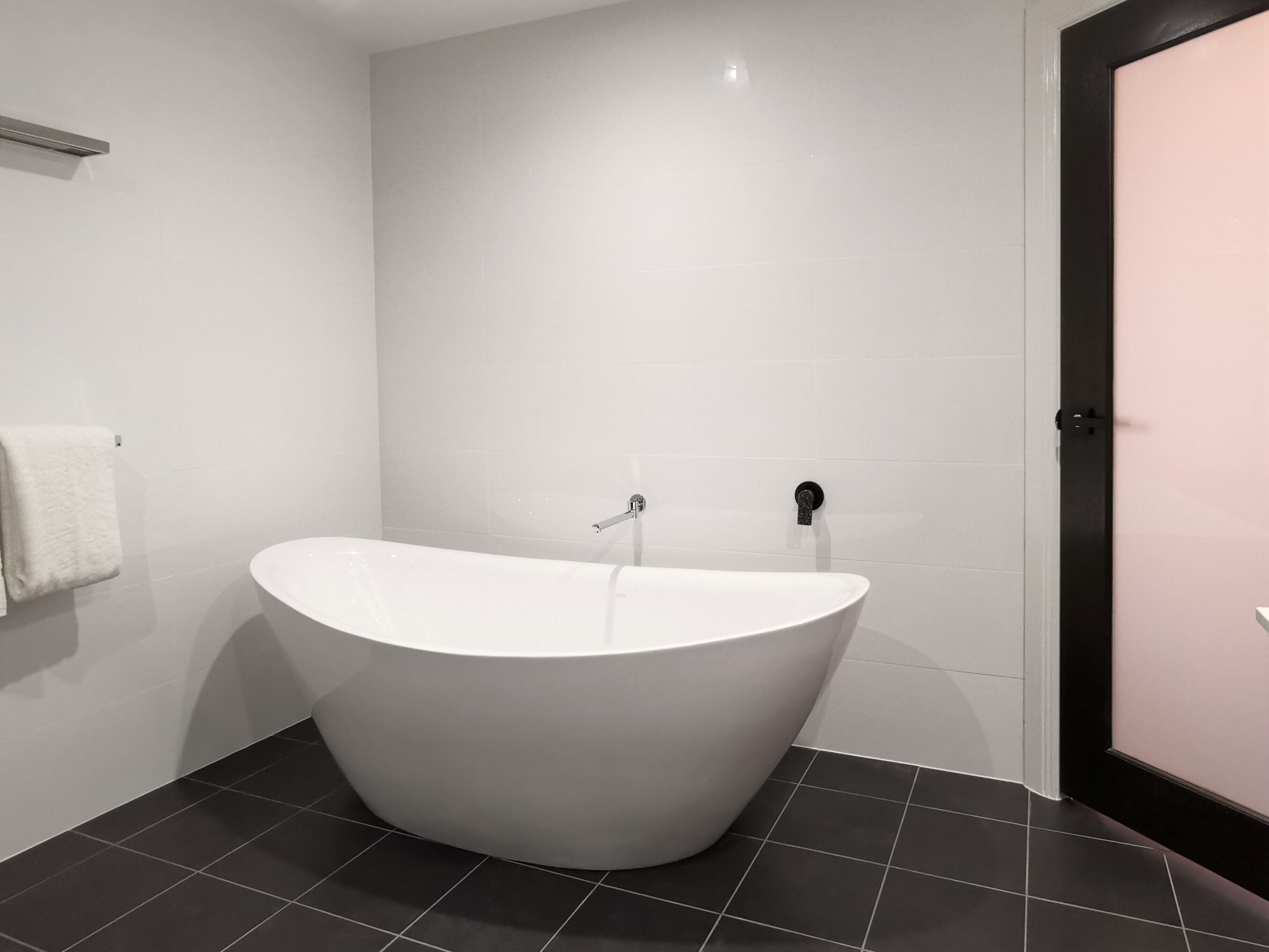 Un baño moderno con una bañera independiente, baldosas blancas y una puerta negra.