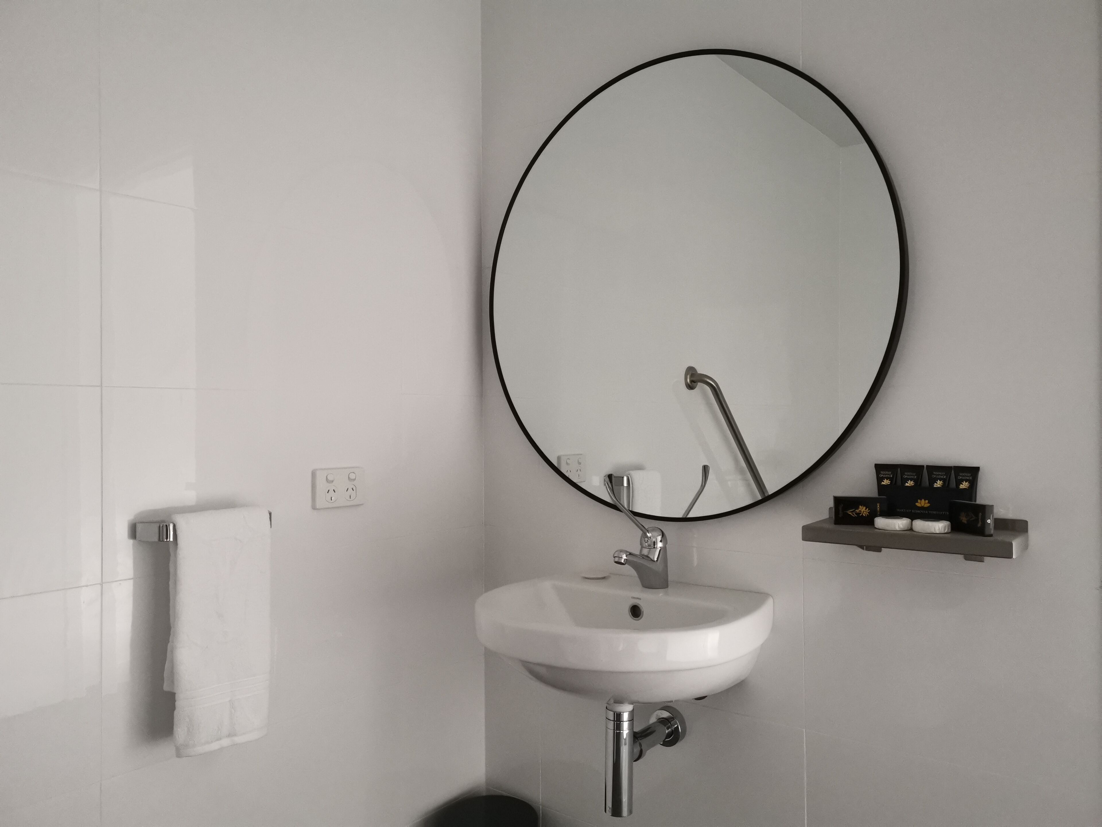 Un baño moderno con un lavamanos blanco, un espejo redondo y un perchero.