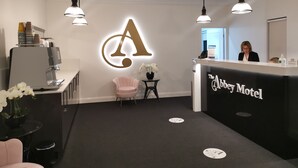 Un espace d’accueil avec un grand panneau lumineux en forme de « A », un comptoir d’accueil, un fauteuil rose et une machine à café.