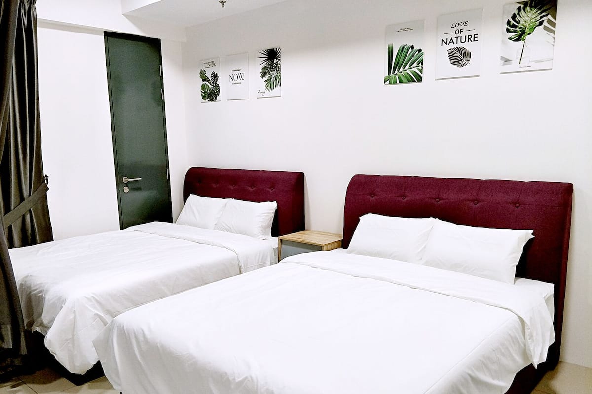 Quarto de hotel com duas camas, cada uma com roupa de cama branca e cabeceira vermelha. Há gravuras botânicas emolduradas na parede e uma mesa de cabeceira de madeira entre as camas.